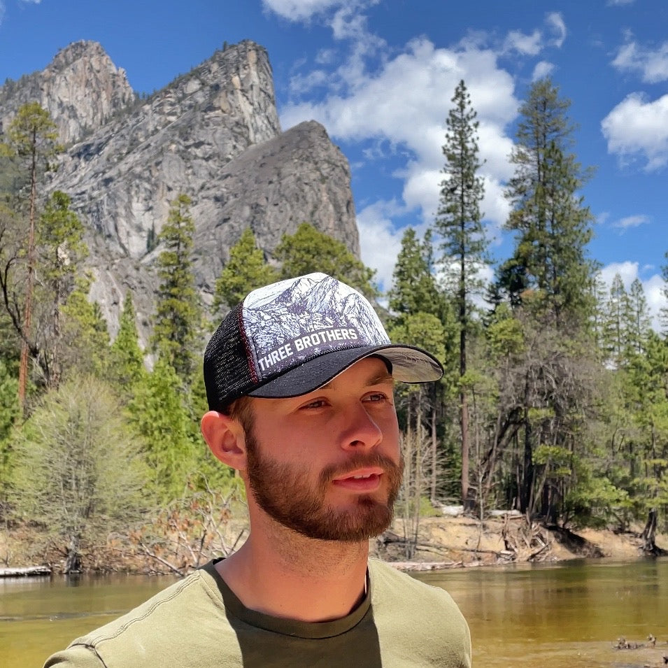 Man wearing a Three Brothers trucker hat in front of Three Brothers mountains  | Hiker Sight